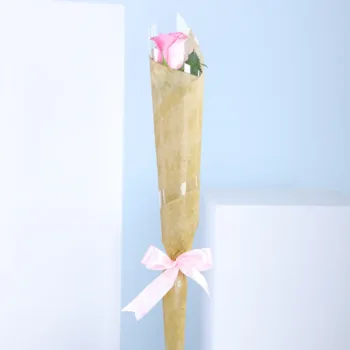 A single pink rose elegantly wrapped in delicate paper, showcasing its soft petals and green stem.