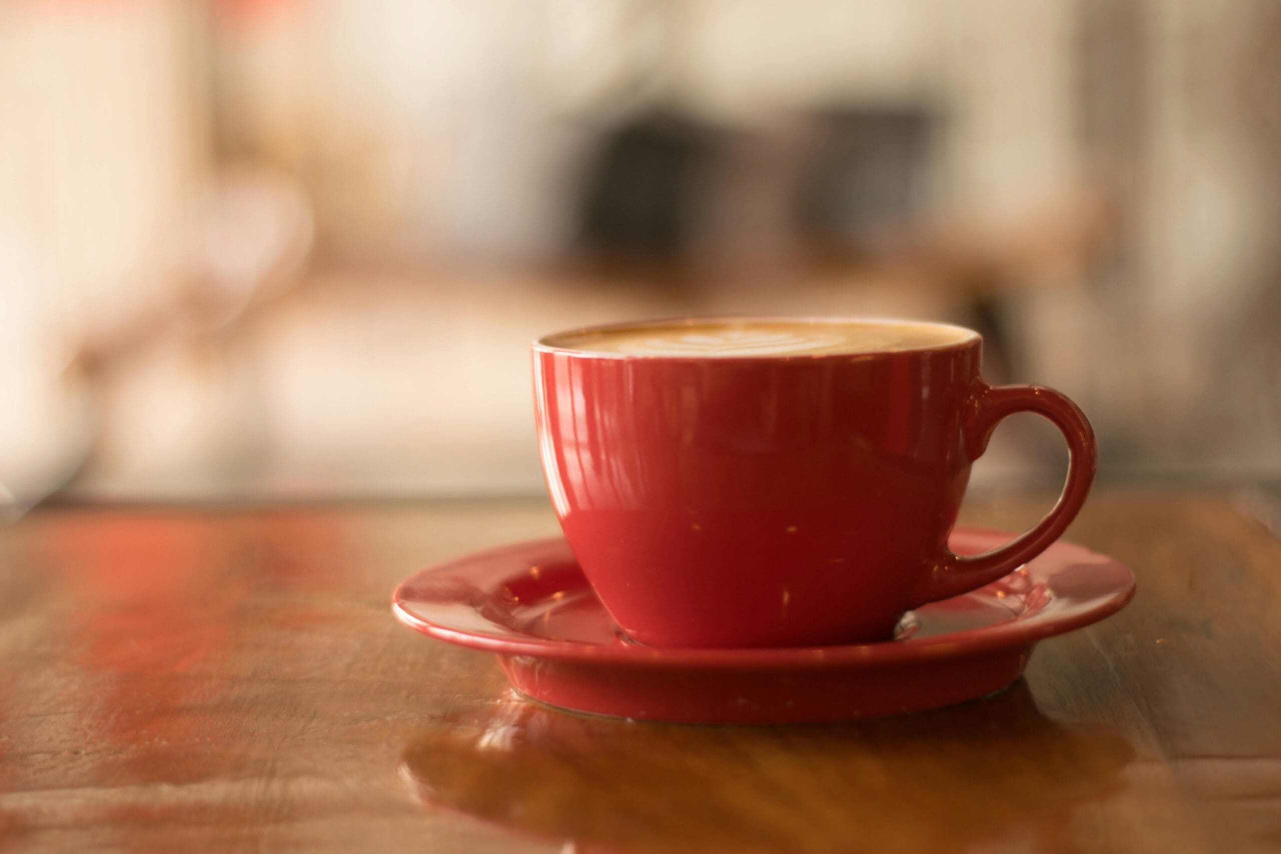 A red coffee cup with latte art sits on a wooden table