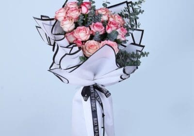 Hand bouquet of blush pink and peach roses with eucalyptus, wrapped in white and black paper.