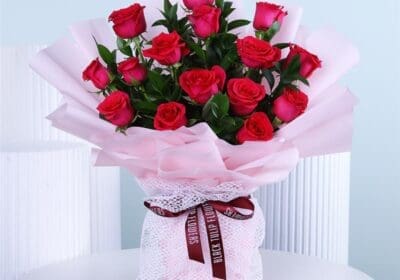 Bouquet of dark pink roses wrapped in soft pink paper with a ribbon placed on a white round table.