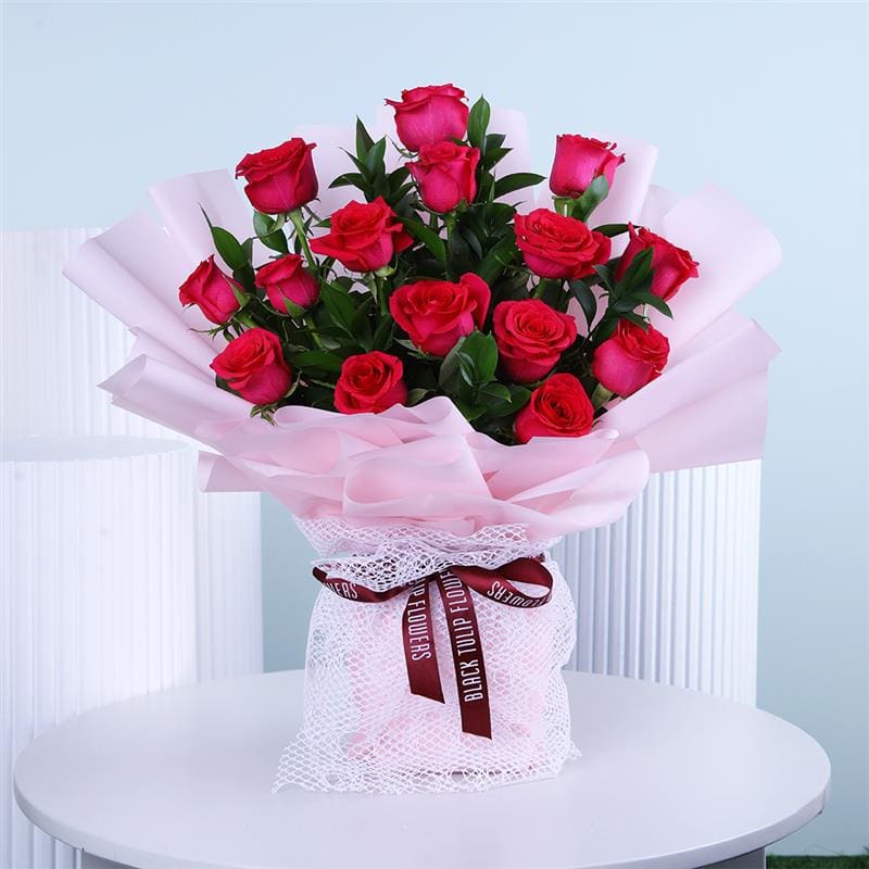 Bouquet of dark pink roses wrapped in soft pink paper with a ribbon placed on a white round table.