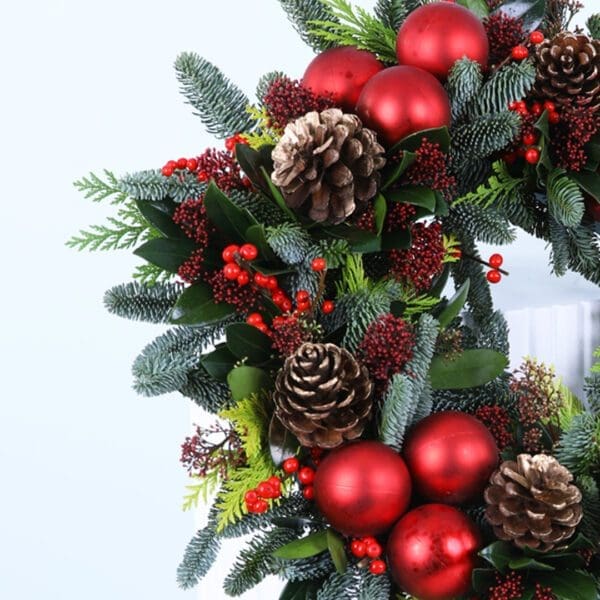 02 Christmas wreath with evergreens, red ornaments, berries, and pinecones on a white stand.