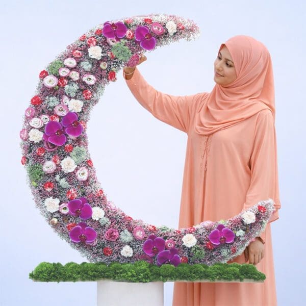 Curved crescent floral box with pastel lisianthus, peach carnations, gypsophilia, green trick stems, and purple orchid in a plywood base.