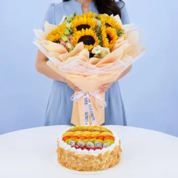 Sunflower Bouquet & Fresh Fruit Cake featuring six vibrant sunflowers, white and peach lisianthus, paired with a colourful 1kg cake topped with assorted fresh seasonal fruits and almond flakes.