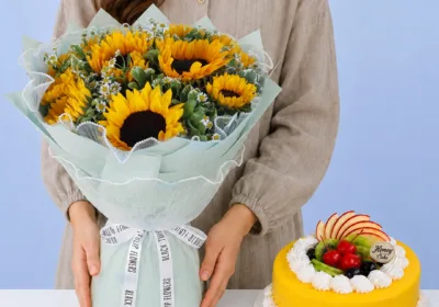 Sunshine Bouquet & Mango Cake Combo featuring fresh sunflowers, Negara and Tanacetum flowers wrapped beautifully with a net cover, paired with a fresh mango cake topped with mango chunks.