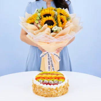 Sunflower Bouquet & Fresh Fruit Cake featuring six vibrant sunflowers, white and peach lisianthus, paired with a colourful 1kg cake topped with assorted fresh seasonal fruits and almond flakes.