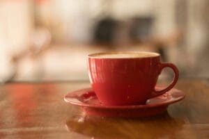 A red coffee cup with latte art sits on a wooden table
