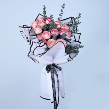 Hand bouquet of blush pink and peach roses with eucalyptus, wrapped in white and black paper.