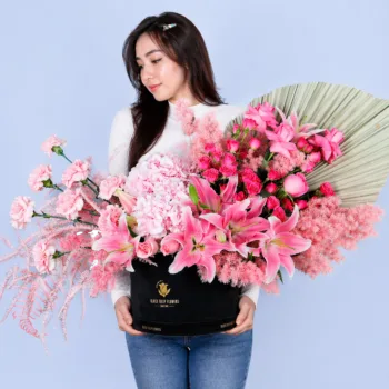 Designer Rose Luxe Box featuring hydrangea, lilies, roses, carnations, and spray roses in soft pink tones arranged in a premium black luxury box with dried foliage accents