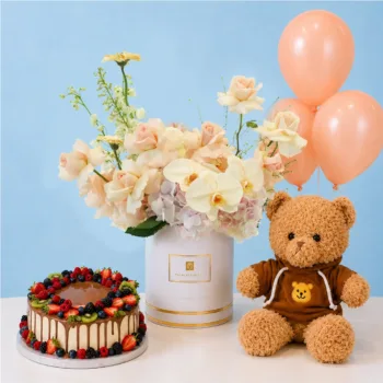 Peach Floral Cake & Teddy Combo featuring peach roses, peach gerberas, light pink hydrangeas, white matthiola, a 1 kg fruit chocolate cake, peach balloons, and a brown hoodie teddy bear in a premium floral hat box.